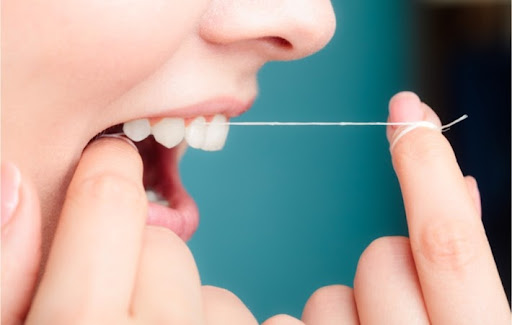 A woman flossing her upper teeth in order to prevent dental health problems
