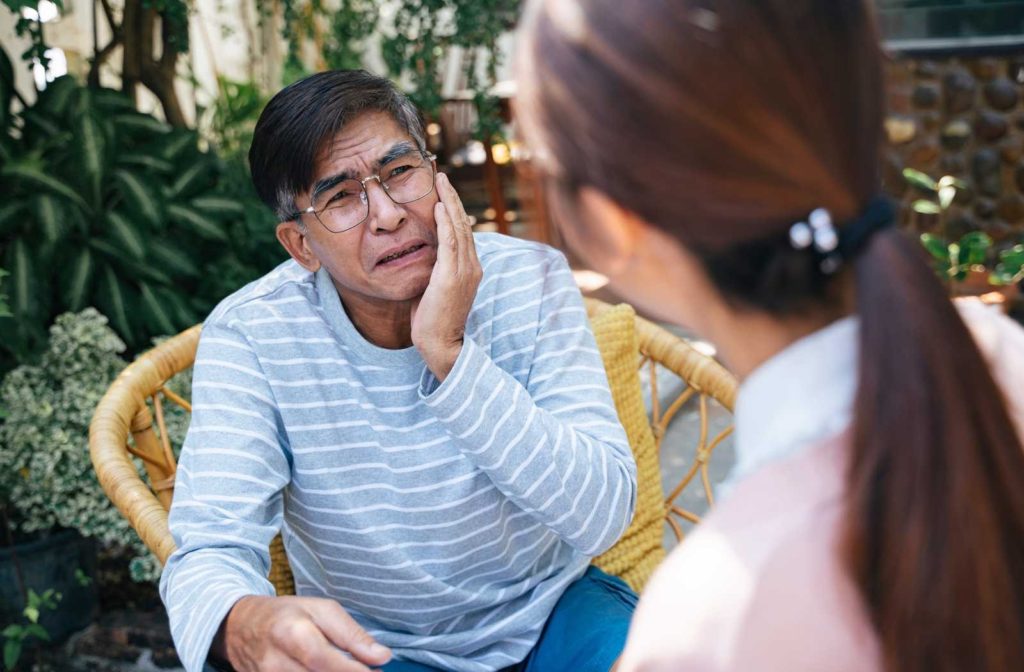 senior man holding jaw and talking to nurse