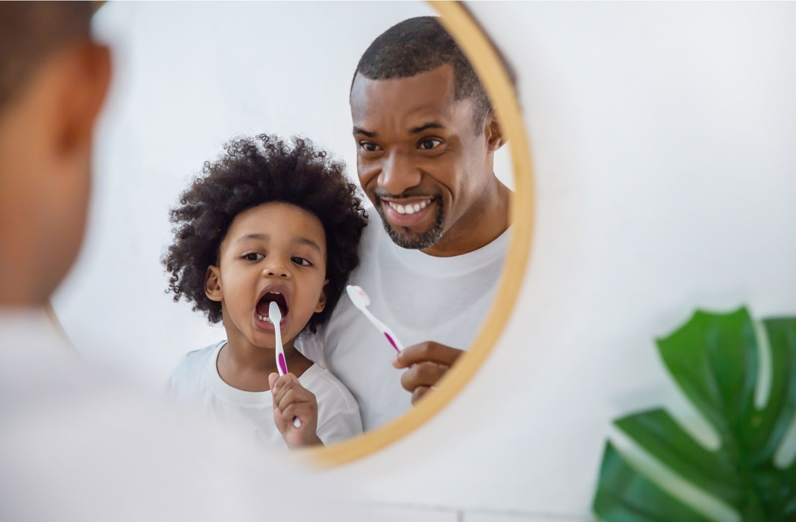 A father and daughter brushing their teeth together in a mirror