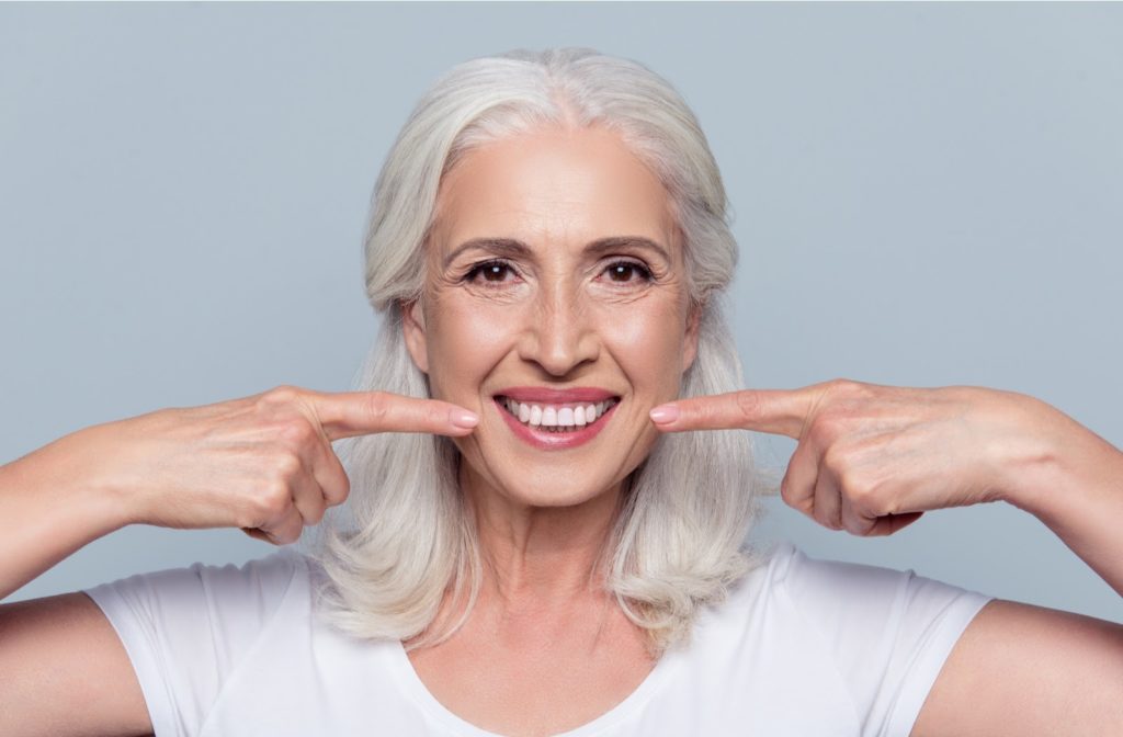 Extremely happy older woman pointing at her clear white teeth with a grey background