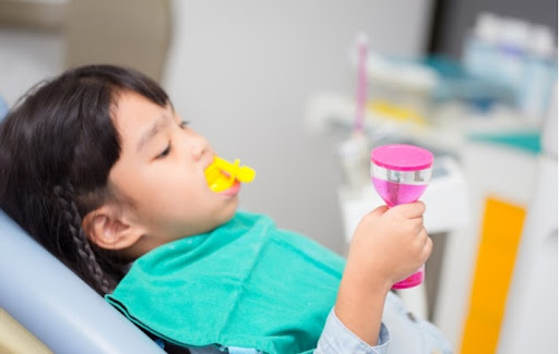 A little girl sitting in a dentists chair waiting while she is receiving a fluoride treatment for her teeth