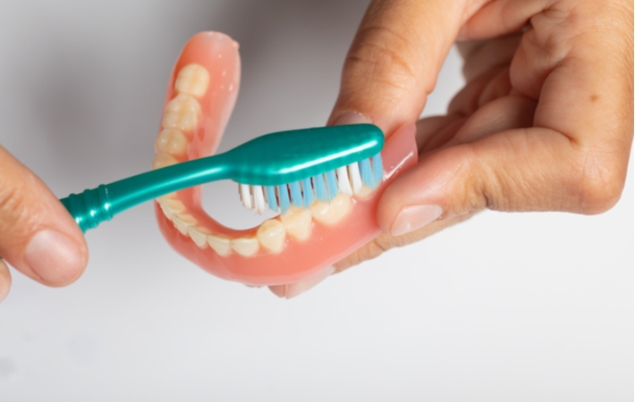 A person using a soft-bristle toothbrush to clean their dentures