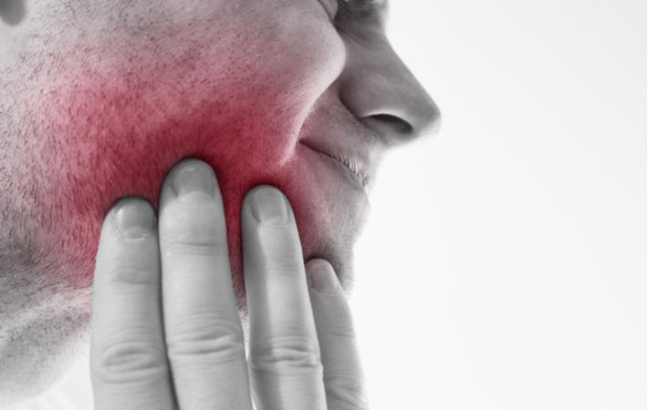 A man holding his cheek highlighted in red to symbolize the pain he feels in his teeth