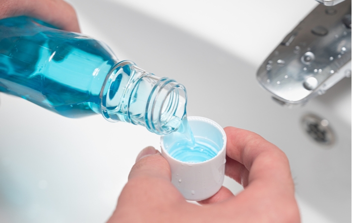 A person pouring blue mouthwash into the bottle's cap over a sink