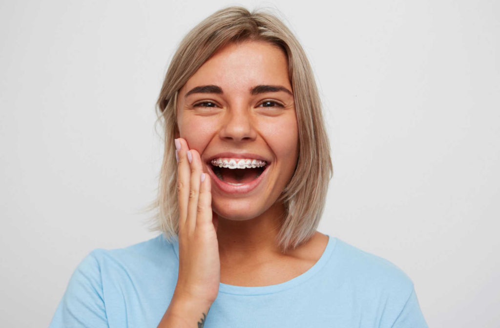 A cheerful young woman, smiling to show off her new braces while she touches the right side of her jaw with her right hand