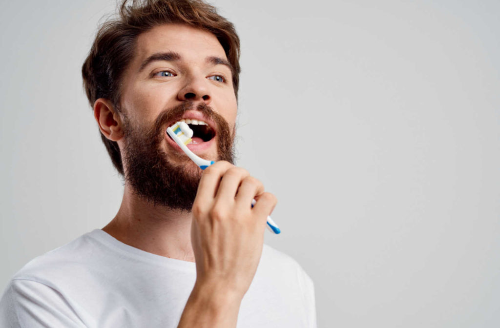A man wearing a white T-shirt holding a toothbrush up to his open mouth, about to begin brushing.