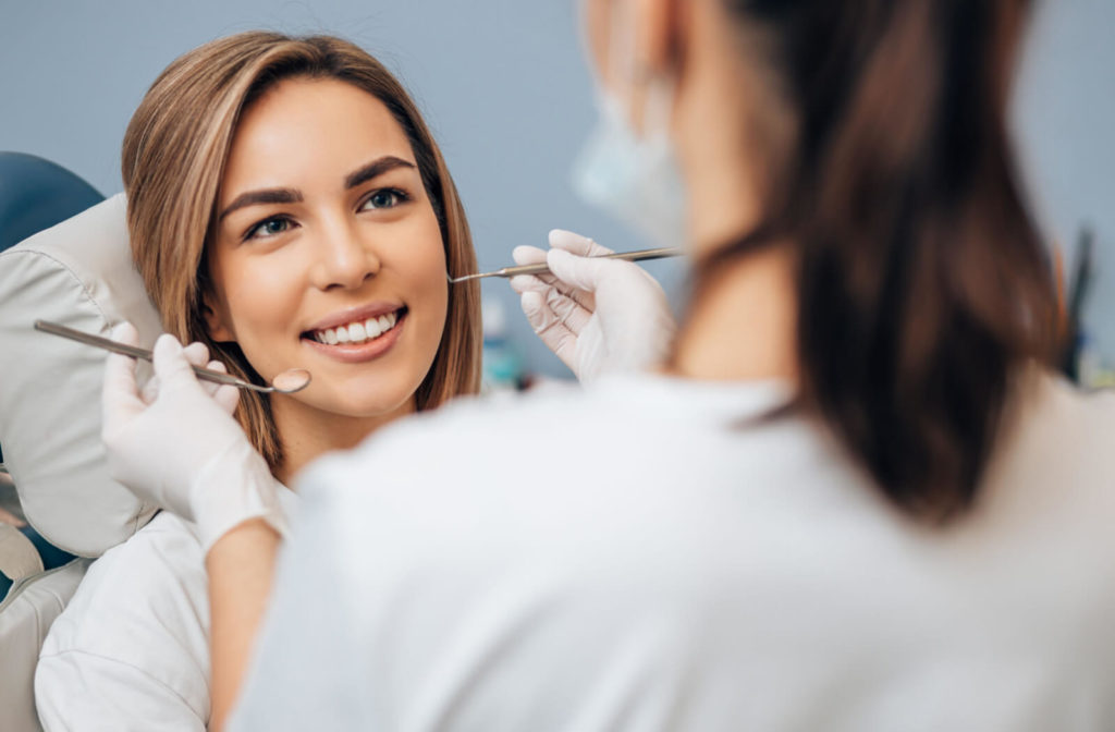 A woman sitting in a dentist's chair while a female dentist examines her teeth for cavities