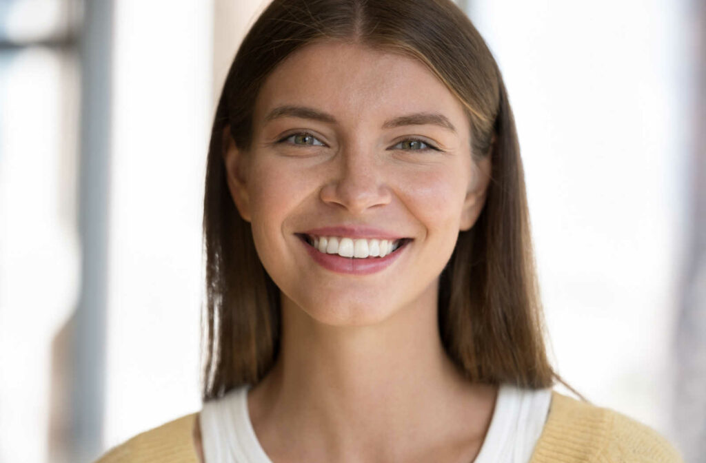 A young woman smiling with white teeth, looking directly at the camera.