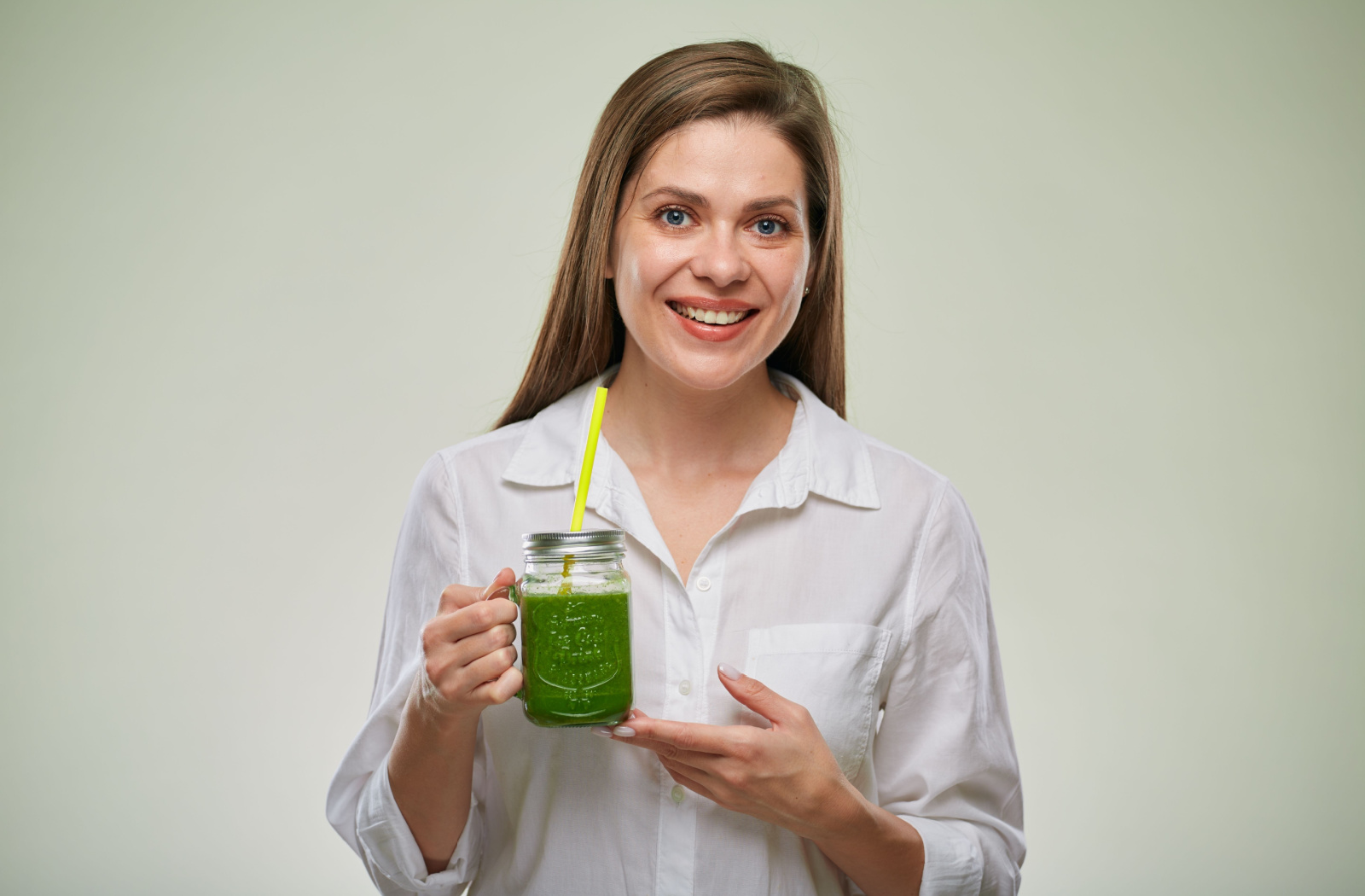 A woman holding a dairy-free fruit smoothie in her right hand as she smiles and looks directly at the camera