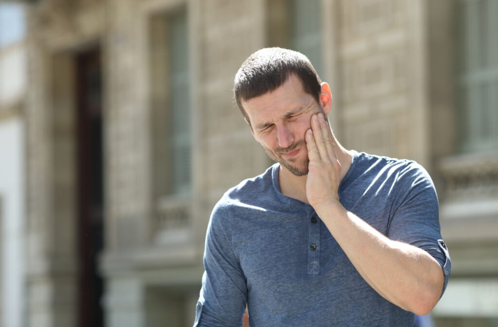 A man suffering from a TMJ holds his right cheek with his right hand.