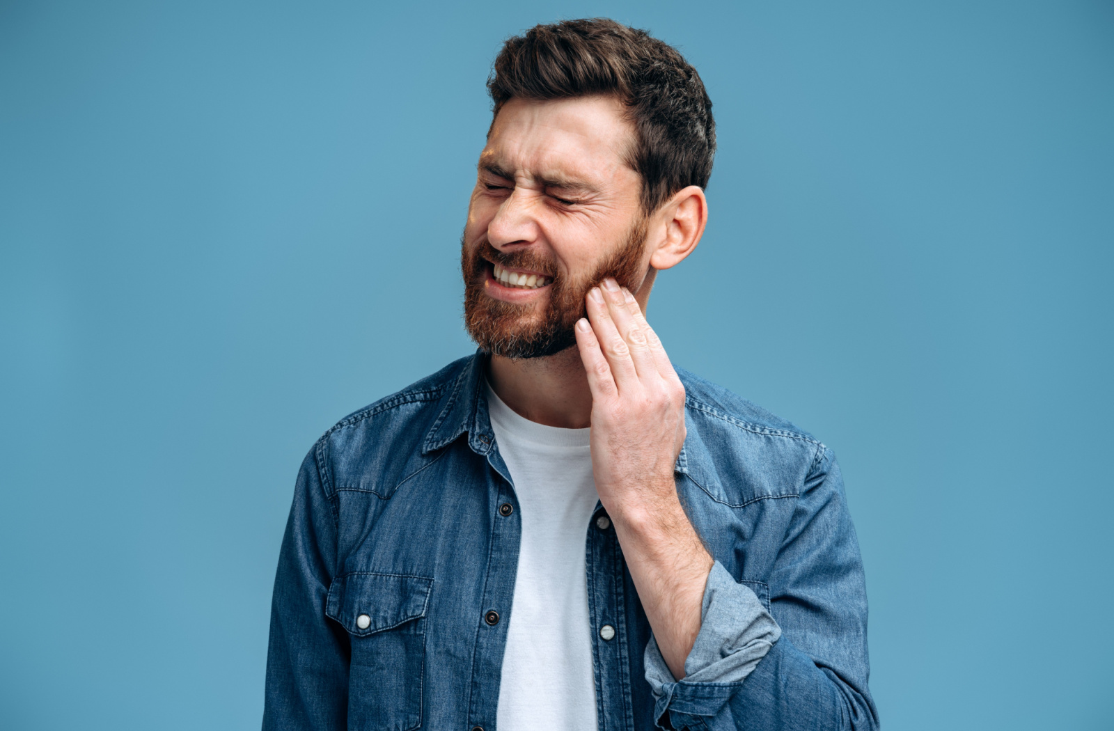 A man suffering from a toothache holds his left cheek with his left hand.