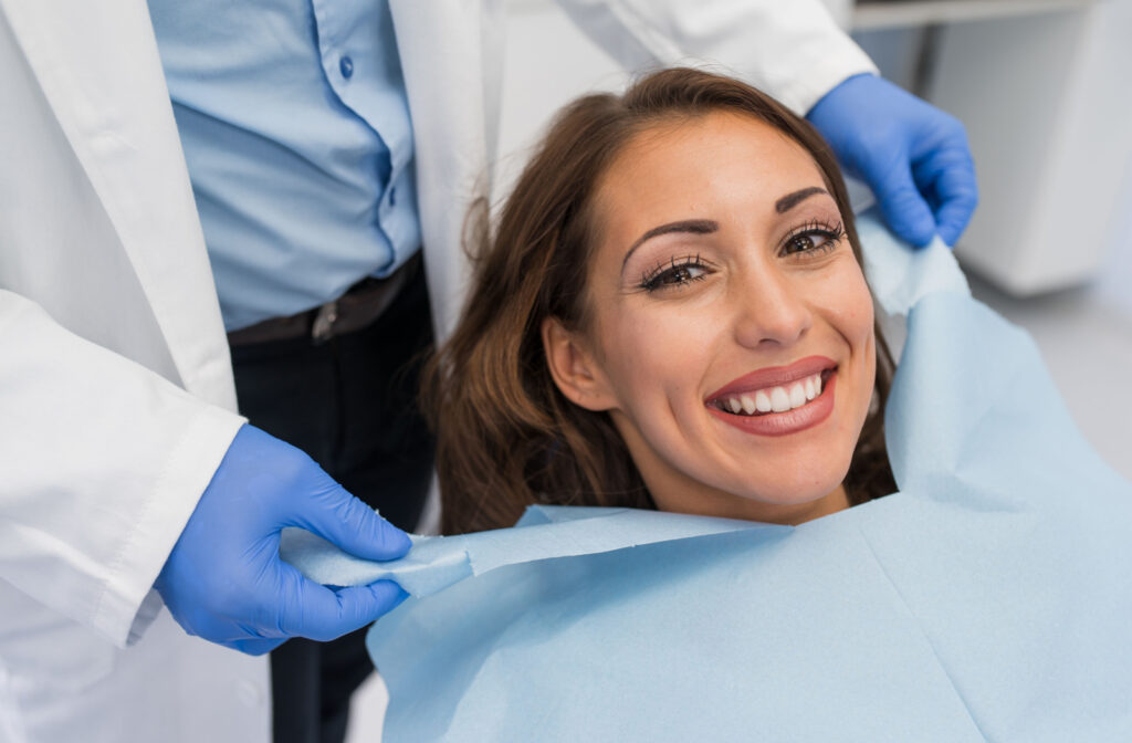 A close-up of a woman smiling while her dentist applies a dental bib