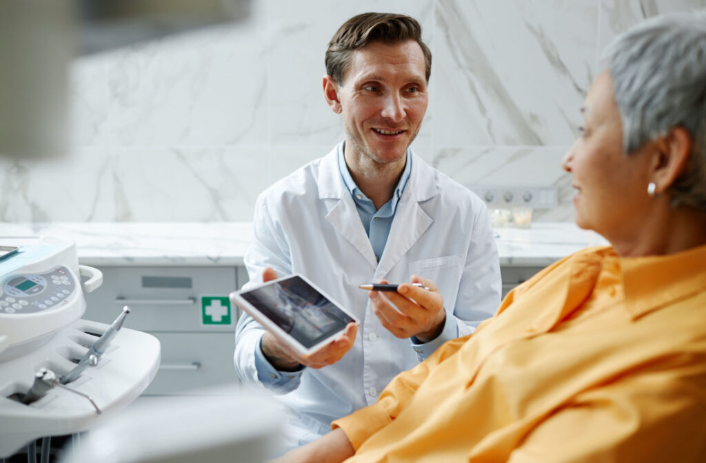 A male dentist holding a tablet and showing it to a woman sitting in a dentist chair
