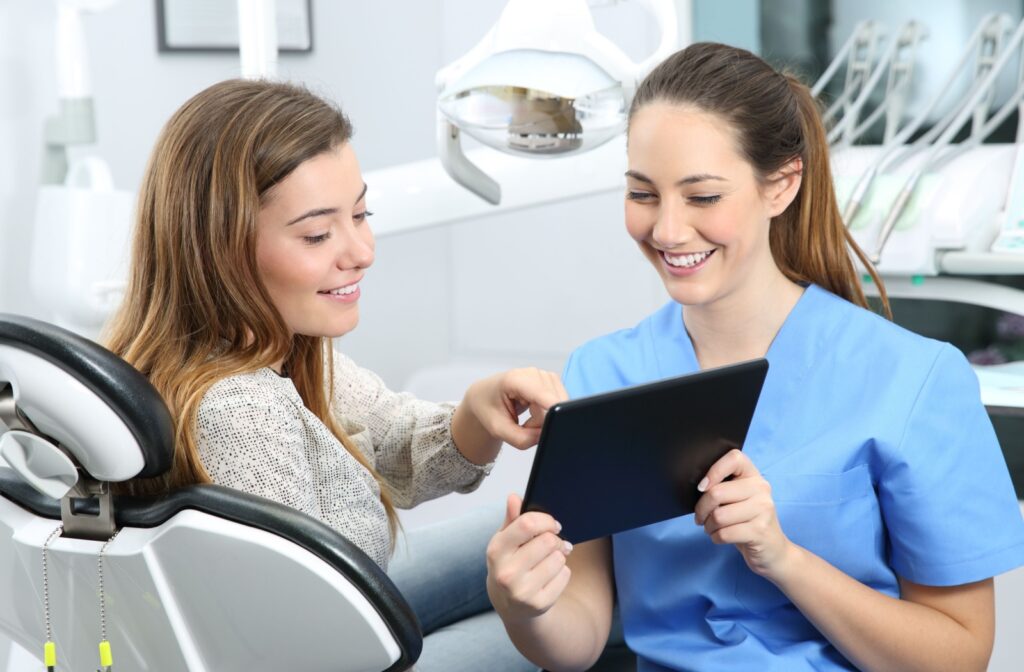 A dentist in blue scrubs holding a tablet talking to their patient about the options for straightening teeth.