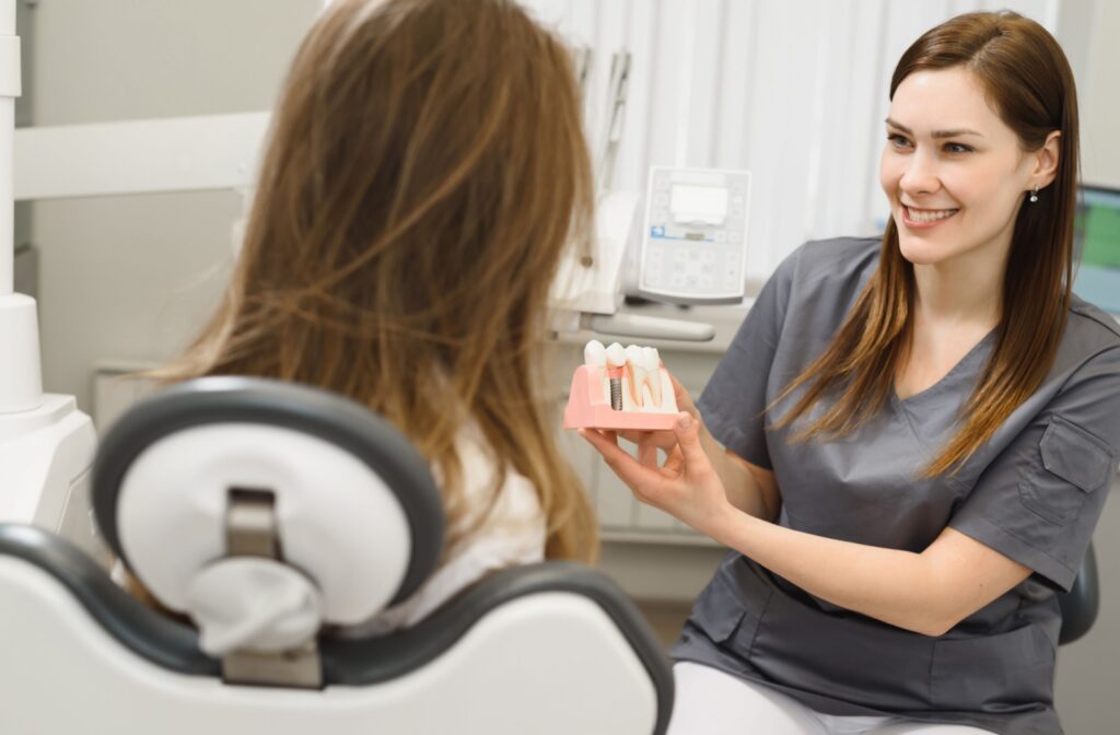 A dentist explaining a dental procedure to a woman while holding an educational tooth model