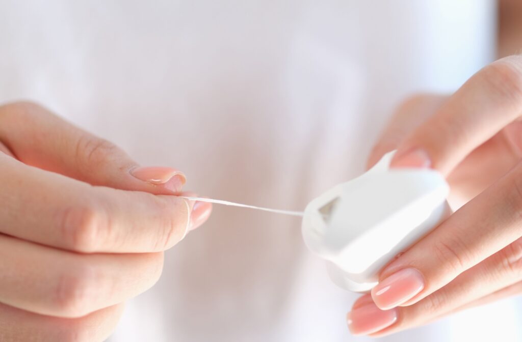 A woman holds a container of floss open in left hand while dispensing a thread of floss with her right hand.
