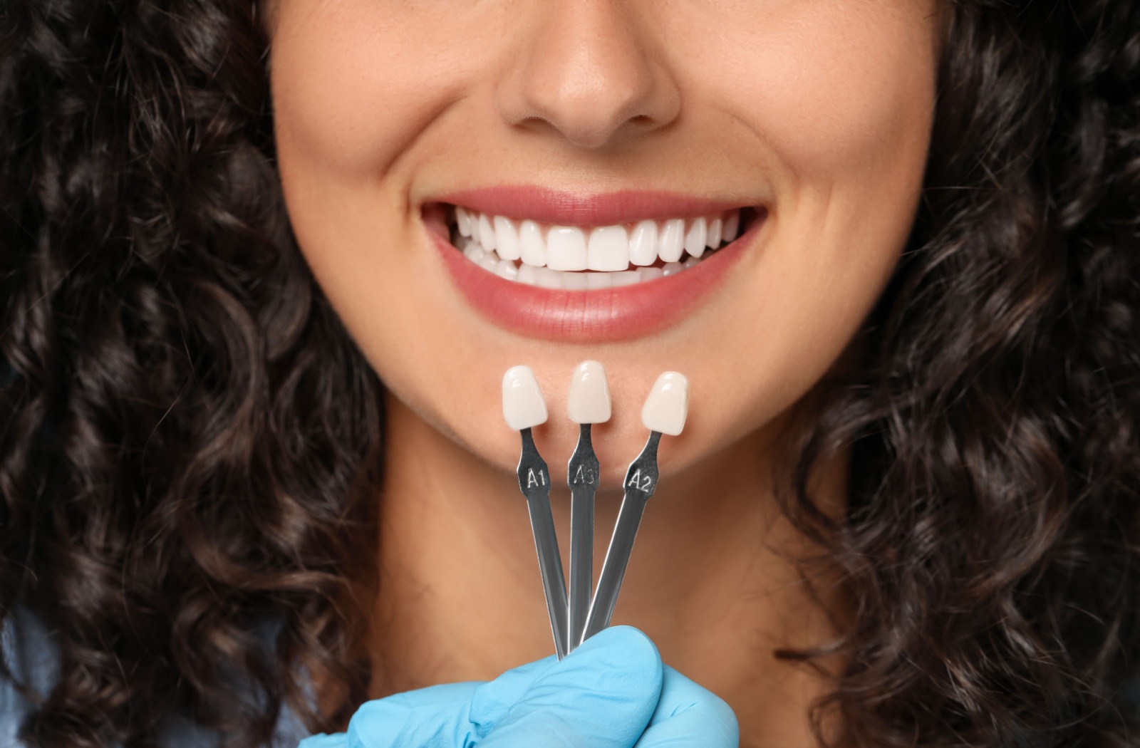 A person smiles while looking in a mirror during a dental visit, with a dentist standing nearby in the background.