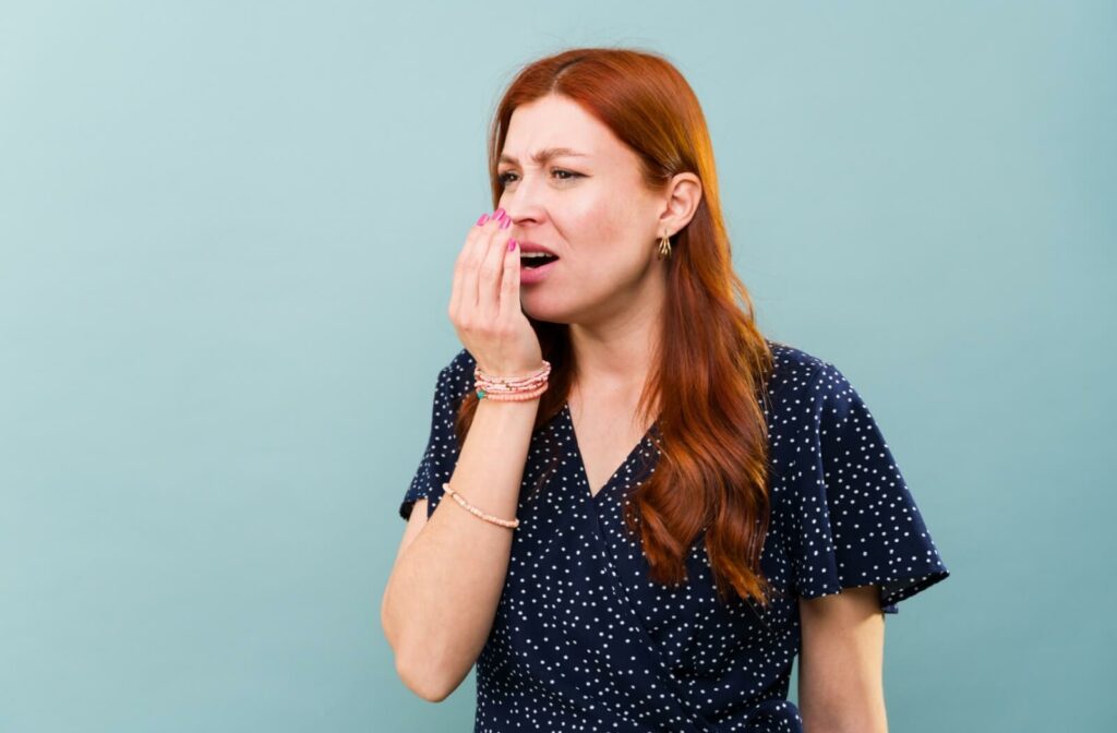 A person cupping their hand over their mouth and breathing into it, looking concerned about having bad breath.