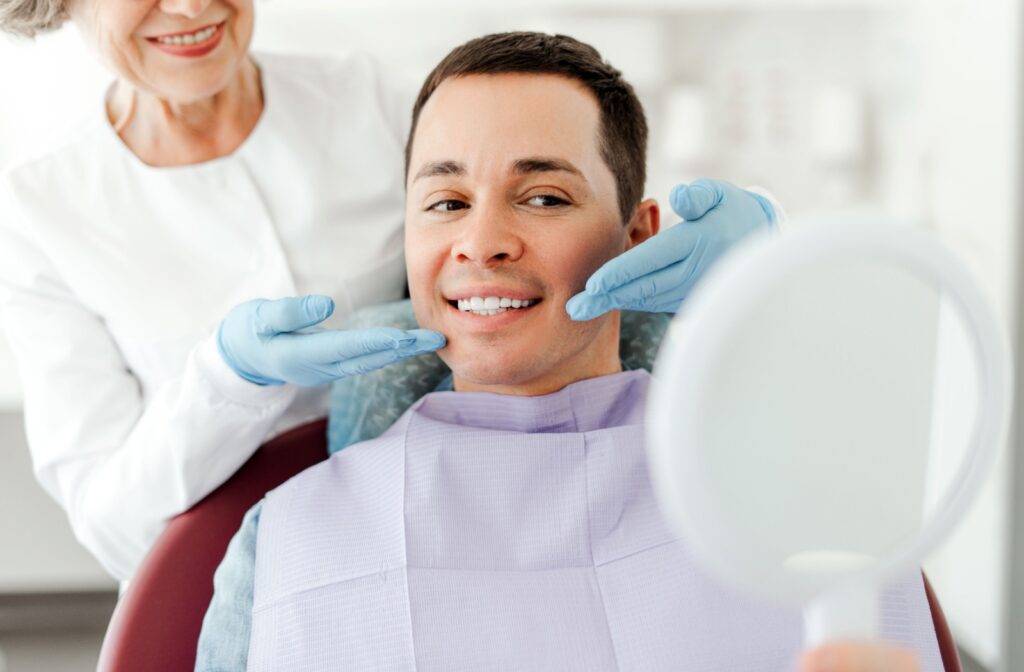 A person sitting in a dental chair and smiling while their dentist frames their smile from behind, explaining the benefits of dental crowns.
