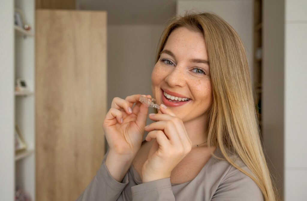 A smiling young adult putting their clear aligners in their mouth.