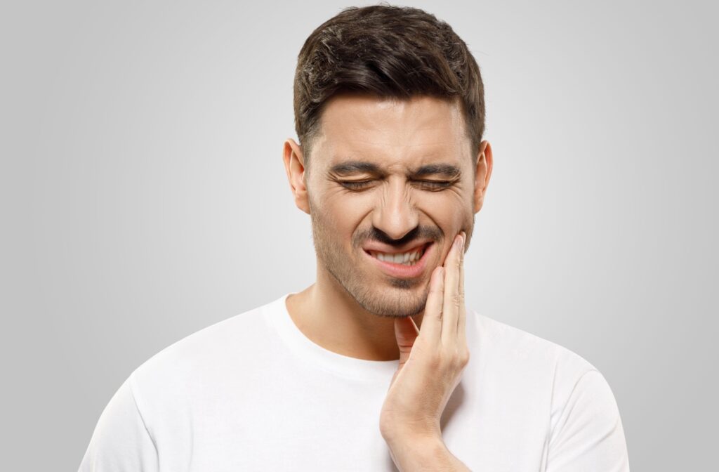 A person winces from jaw pain and tries to soothe the area with their hand.