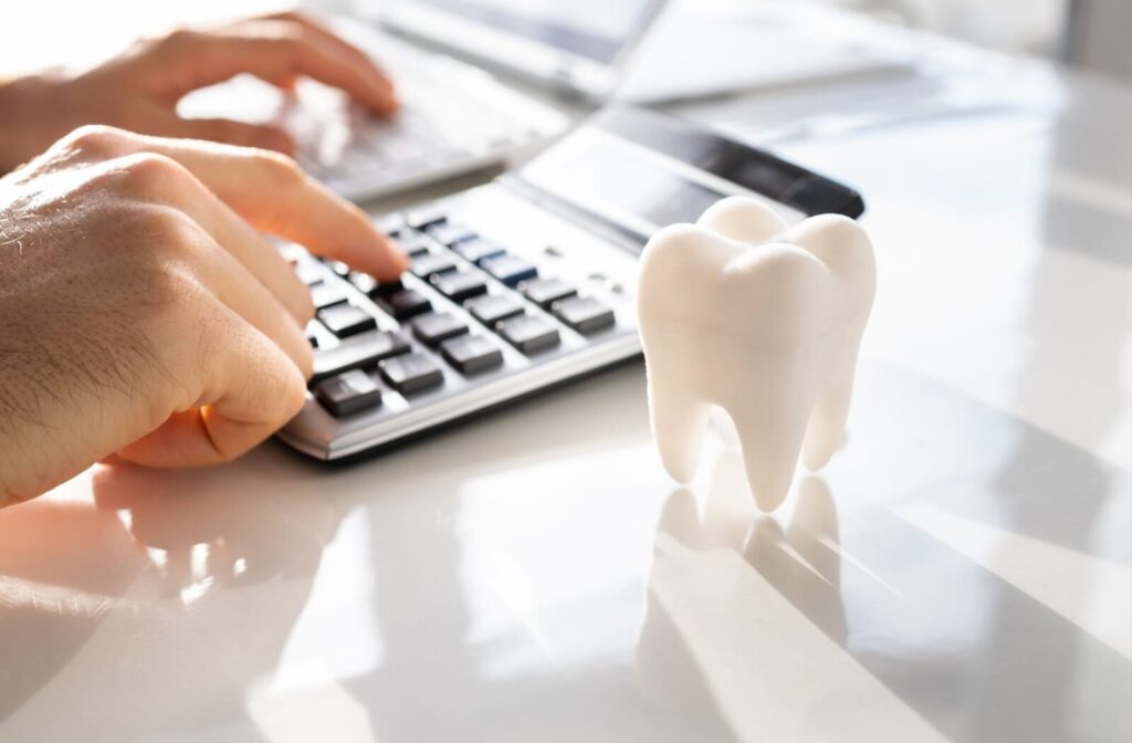 A person uses a calculator at a desk with a tooth-shaped model placed beside it.